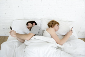 un couple au lit dos tourné avec leurs smartphones en plein problème de communication